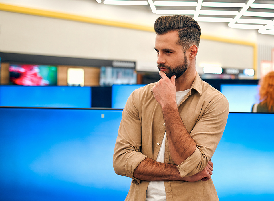 Foto: En man i en tv-butik kliar sig i skägget och ser fundersam ut.
