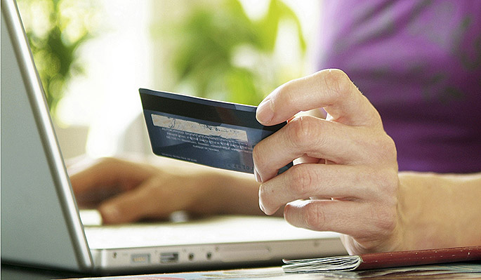 Foto: närbild på en kvinna som håller i ett bankkort och skriver på en dator
